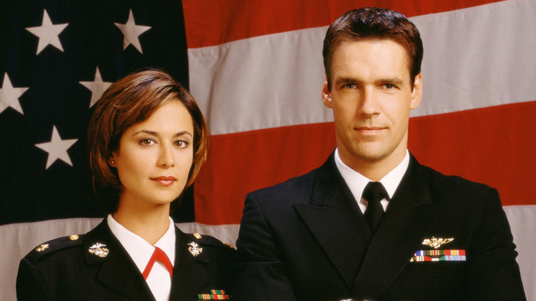 Catherine Bell as Sarah 'Mac' Mackenzie and David James Elliot as Harmon 'Harm' Rabb Jr. stand in front of the Stars and Stripes in uniform in JAG