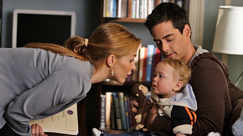 Adam Kaufman holding a baby as Poppy Montgomery leans in