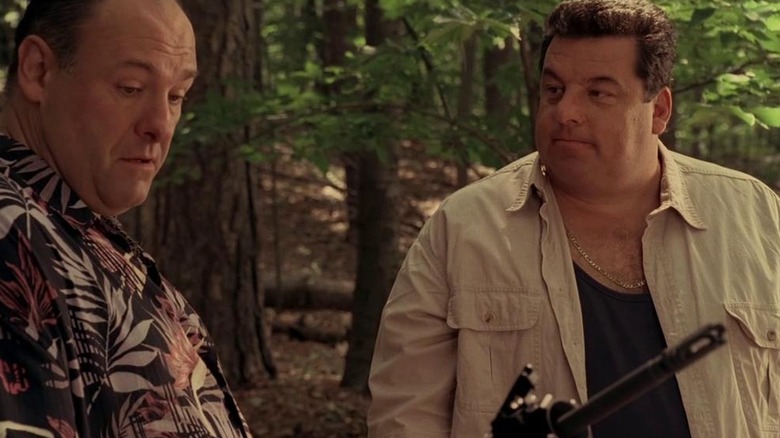 Tony holds an automatic gun while standing with Bobby