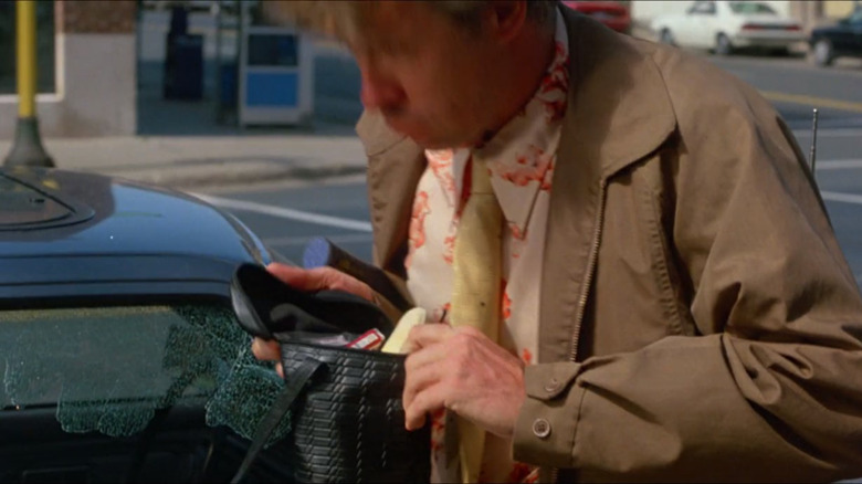 a man inspects a purse next to a broken car window