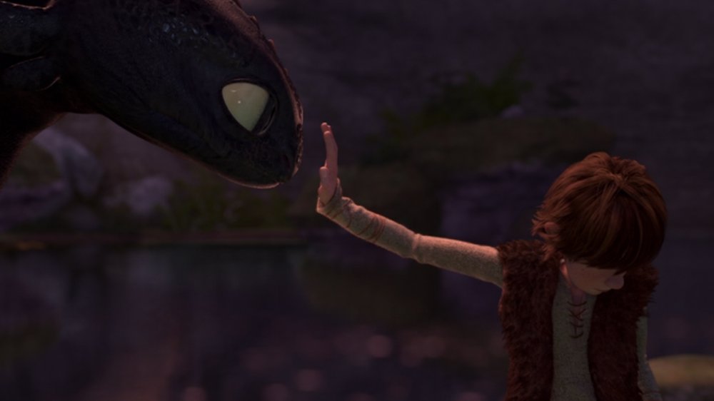 A teen boy (Hiccup), reaches out his hand tentatively towards the head of a black dragon (Toothless). A scene from the movie How to Train Your Dragon. 