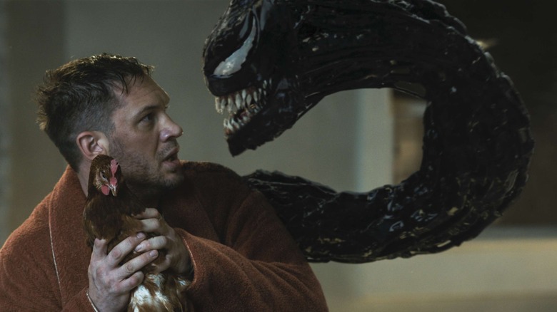 Eddie Brock holds a chicken while facing off against Venom