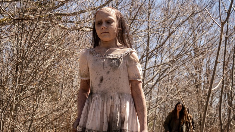 A cursed child walking in front of Tabitha in woods in From