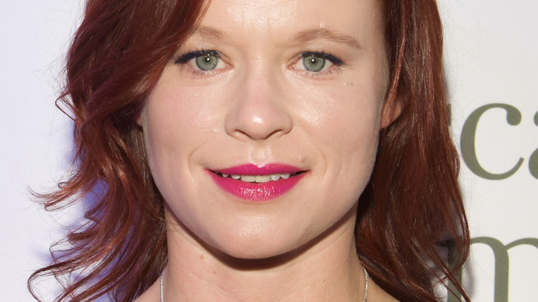 Thora Birch smiling at a press event, in pink lipstick and black eyeliner