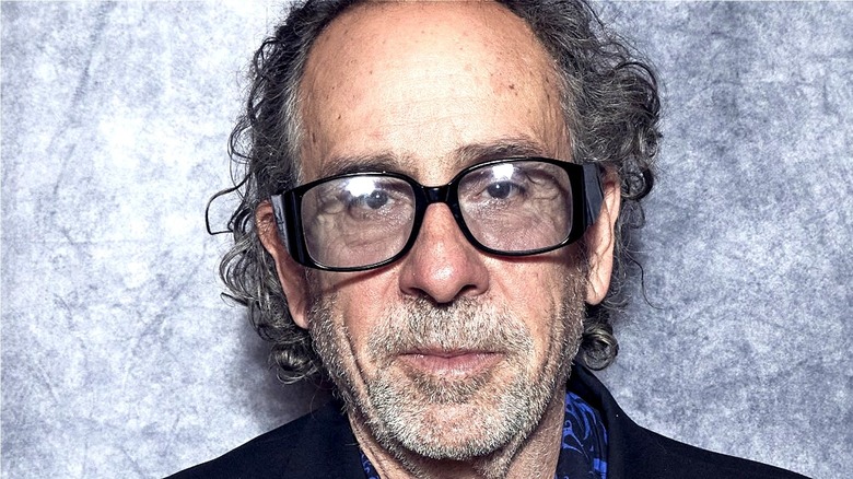 Tim Burton wearing big glasses with heavy stubble and disheveled hair