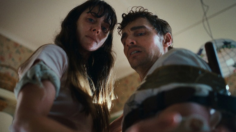 Millie and Tim (who's strapped to a chair) look downward in 