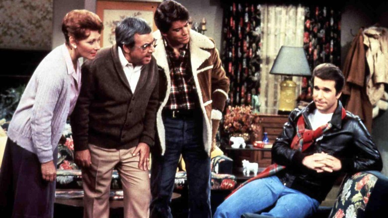 Marion, Howard, and Potsie stand over Fonzie, sitting on a recliner in Happy Days