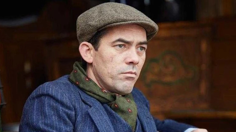 Johnny Dogs wearing a blue suit and a cap on "Peaky Blinders" (2013-2022)