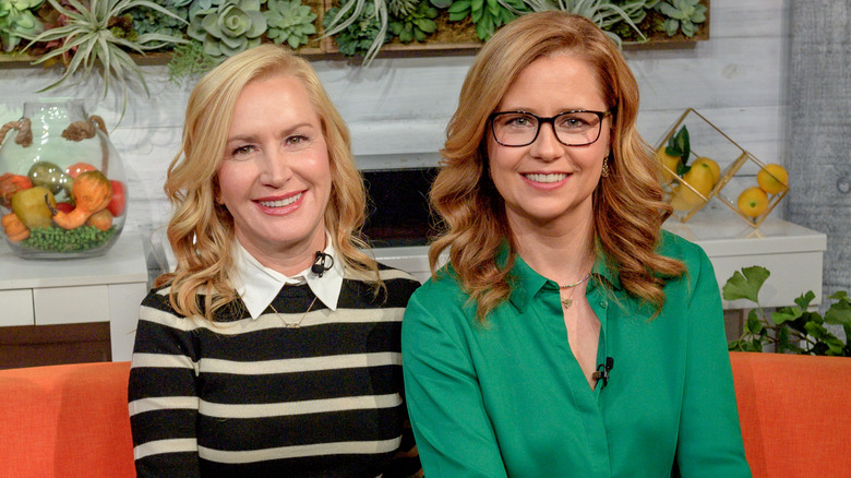Angela Kinsey and Jenna Fischer smiling together on couch
