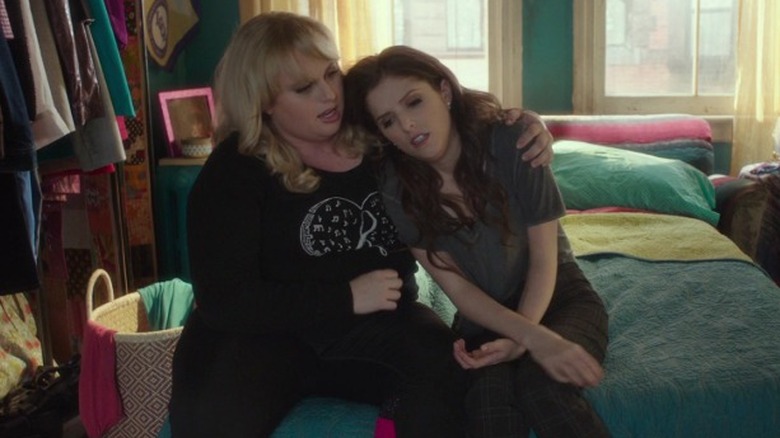 Becca Mitchell sitting on a bed and resting her head on Patricia "Fat Amy" Hobart's shoulder in Pitch Perfect 3 (2017)