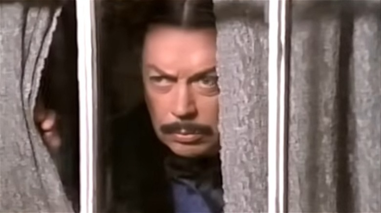 Gomez Addams peeking through a curtain and looking out the window in Addams Family Reunion (1998)