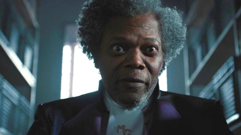 Mr. Glass sitting between two rows of shelves in Glass (2019)