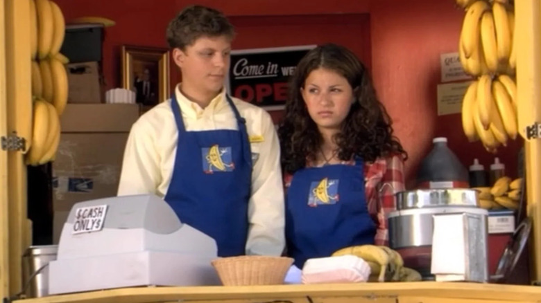 Michael Bluth and Maeby Funke stand behind the counter of the banana stand wearing blue aprons in "Arrested Development"