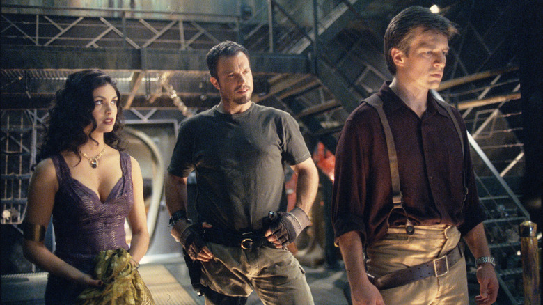 Mal Reynolds stands dejected while Jayne Cobb holds his hands on his waist and Inara Serra stand behind him in "Firefly"