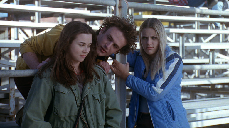 Nick Andopolis whispers into the ear of Lindsay Weir while Kim Kelly watches skeptically under the bleachers of 