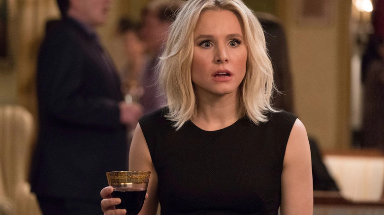 Eleanor holds a glass of wine with a shocked expression on her face.