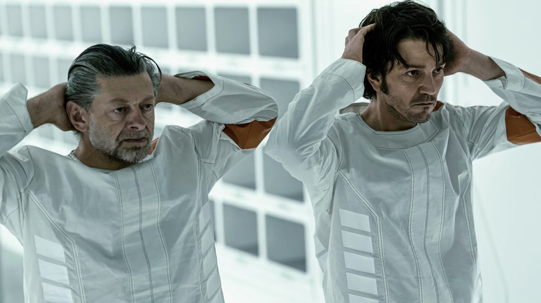 Cassian Andor and Kino Loy in matching white uniforms hold their hands behind their heads in "Andor" (2022-2025)