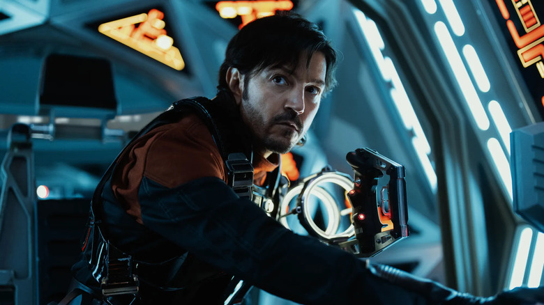 Cassian Andor sits in the cockpit of a Tie Interceptor in an orange jumpsuit in 