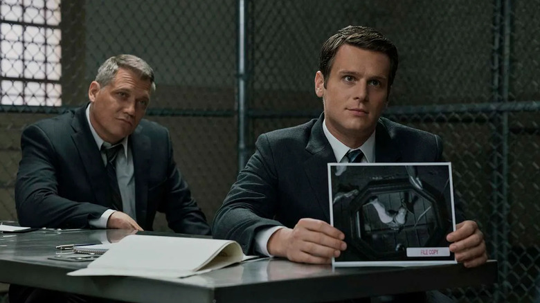 Holden Ford holds a crime scene photo while Bill Tench sits behind him inside a prison in "Mindhunter" (2017-2019)