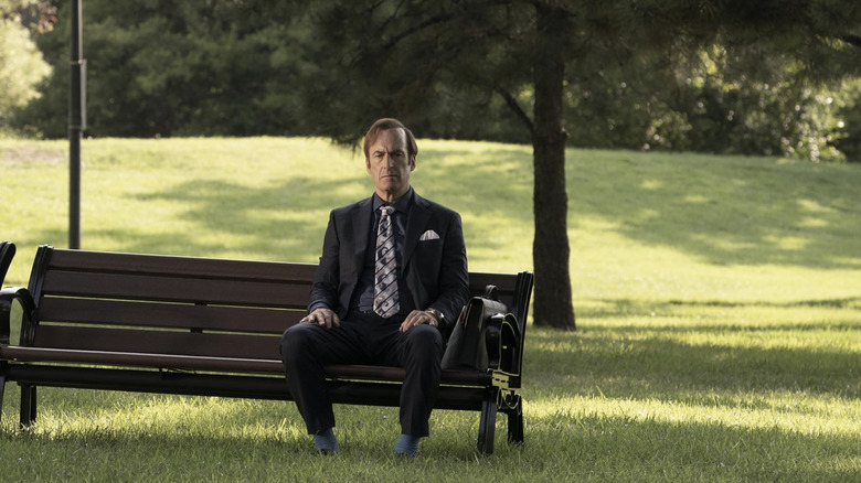 Saul Goodman in dark suit sitting on park bench