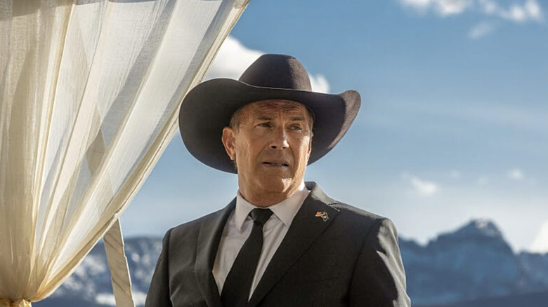 John Dutton in dark grey suit and hat standing outdoors