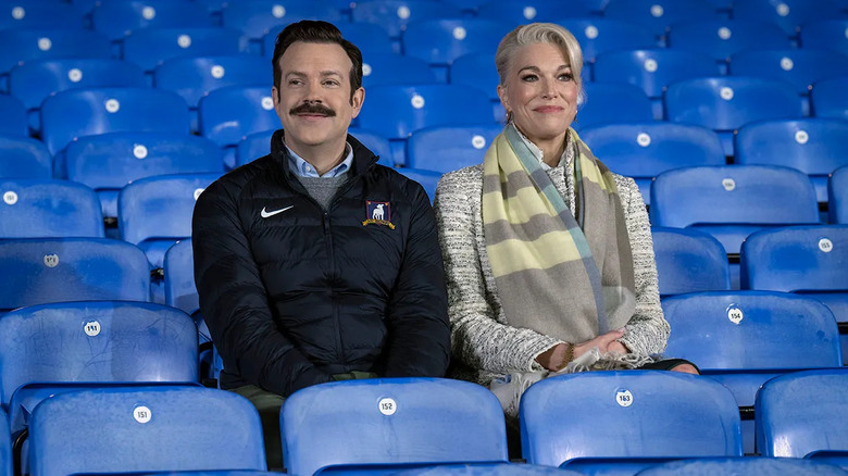 Ted and Rebecca sitting in the stands and smiling on Ted Lasso