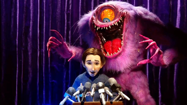 A one-eyed monster standing behind a man at a podium in The Shivering Truth