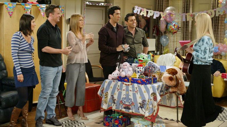 The cast of Friends standing in Chandler and Joey's living room during Emma's first birthday