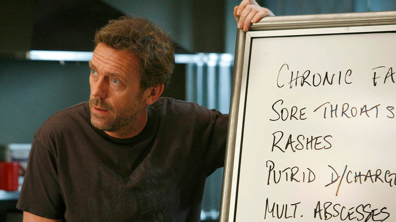 Dr. House standing next to his whiteboard reviewing ideas with his off-camera team in House, M.D.