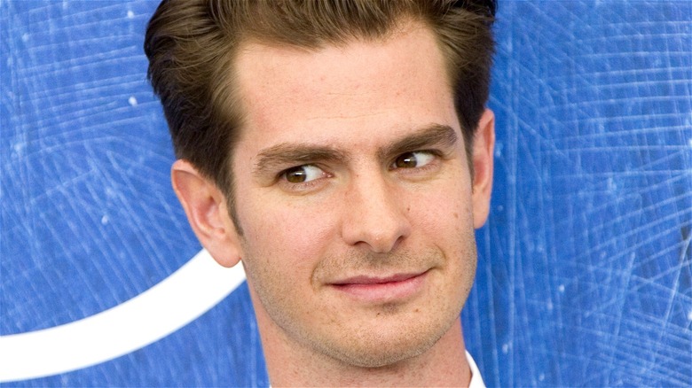 Andrew Garfield looking sideways with blue background