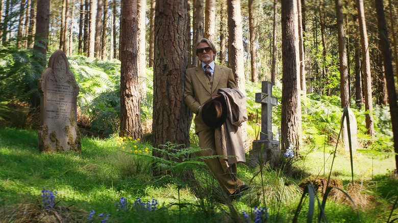 Benoit Blanc leans on a tree in a graveyard in 