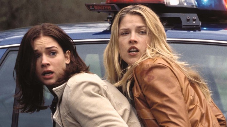 Two friends taking cover next to a cop car in Final Destination 2