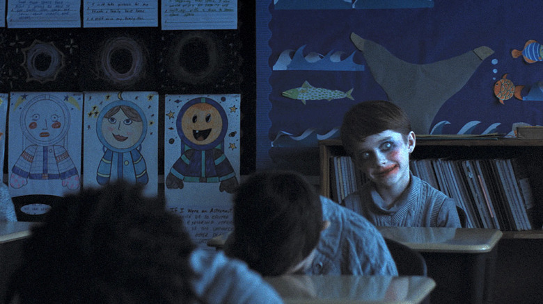 Alex smiling creepily with clown makeup on in the classroom in Weapons