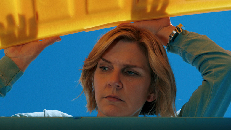 Carol lifting a trashcan lid and looking inside in Pluribus