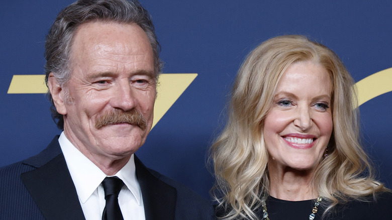 Bryan Cranston and Anna Gunn smiling for photos in front of blue backdrop in 2024