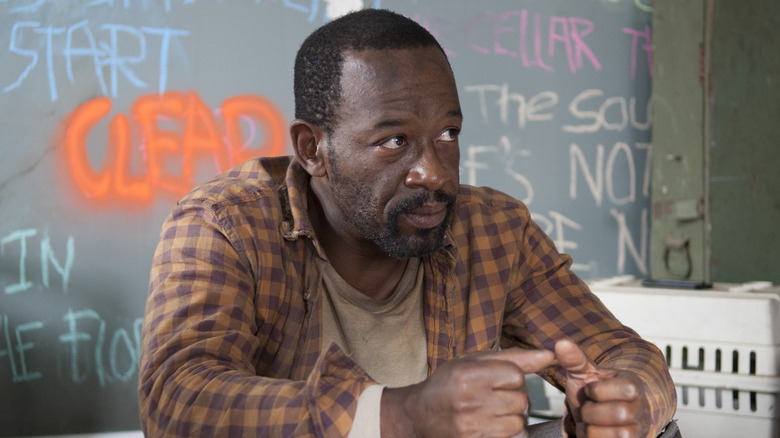 Morgan Jones sitting in his house with a wall covered in scribbles in the background (2013)