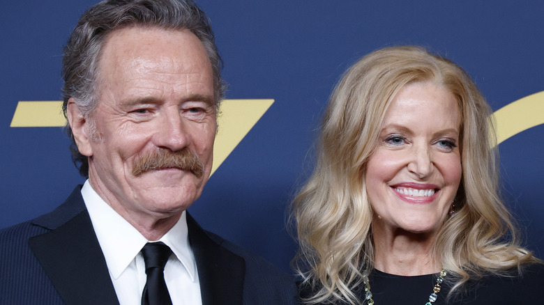 Bryan Cranston and Anna Gunn smiling for photos in front of blue backdrop in 2024