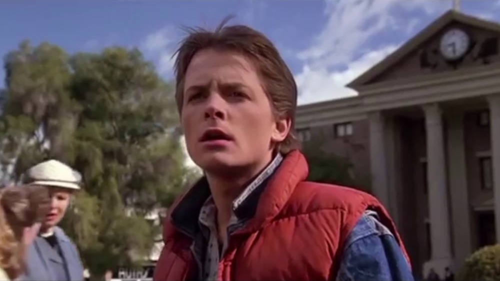 Michael J Fox as Marty McFly in puffy coat in front of clock tower in Back to the Future