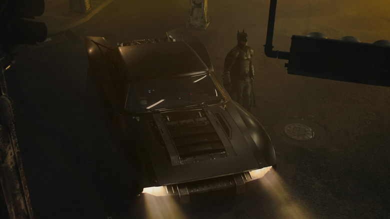 Batman next to Batmobile in Gotham City at night