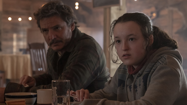 Pedro Pascal and Bella Ramsey in The Last of Us sitting at table with curious faces