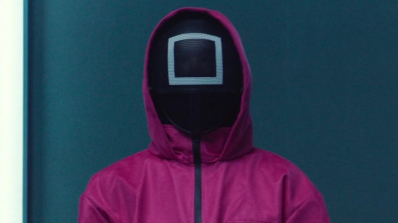 A pink guard stands in front of a gray wall in Squid Game (2021-2025)