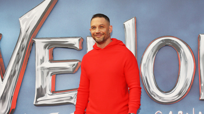 Tom Hardy beams against a promo backdrop for Venom