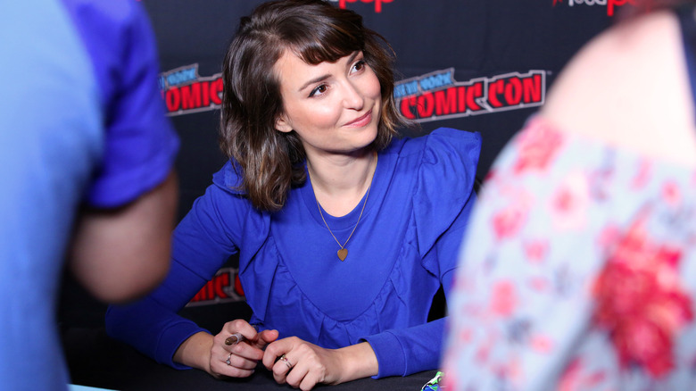 Milana Vayntrub tersenyum di meja di Comic-Con