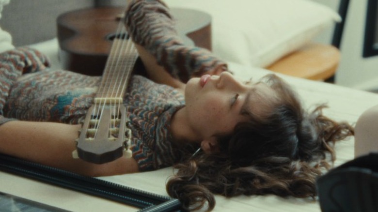 Frances Anderson lying on a couch with a guitar fretboard over her in the Don't Forget Me music video