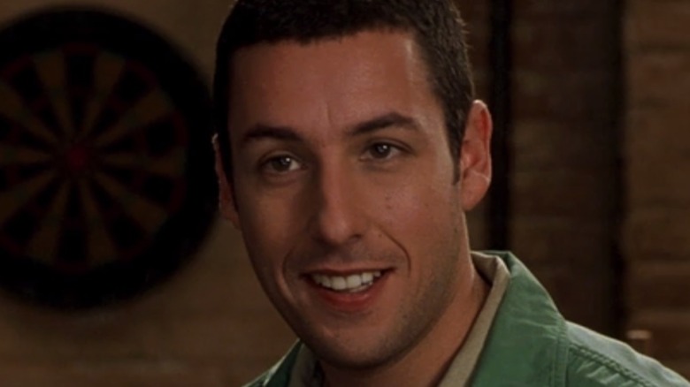 Adam Sandler smiling in close-up with a dartboard in the background