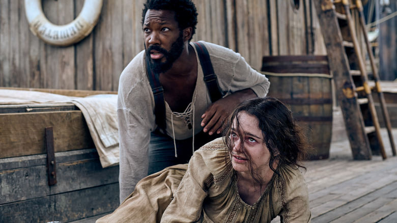 Corey Hawkins kneels behind Aisling Franciosi