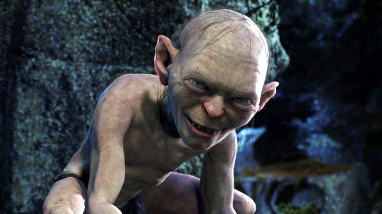 Gollum smiling and crouching by a stone wall