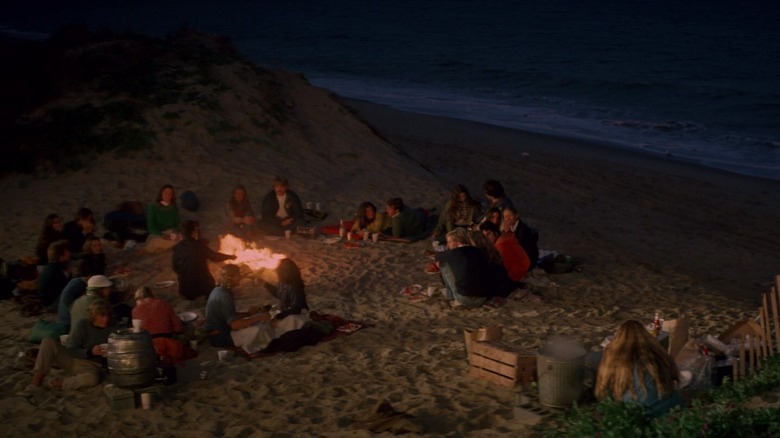 Tom and Chrissie in "Jaws" sat across from each other on the beach with fire and other couples in background
