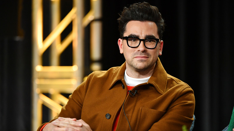 Dan Levy sitting with hands crossed