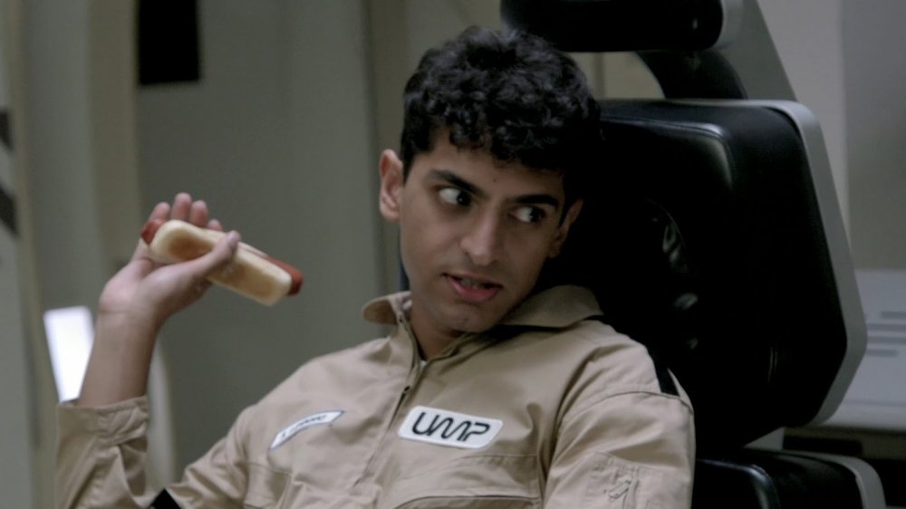 Karan Soni as Stewart Lipinski, eating a hotdog, on Other Space